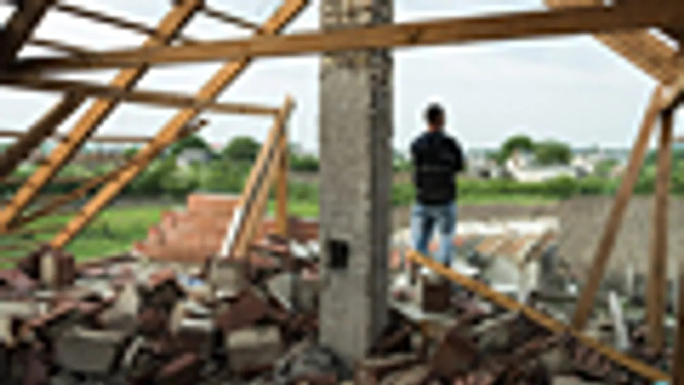 szélvihar, viharos erejű szél, viharkár, Egy férfi áll megrongálódott háza tetején a Szabolcs-Szatmár-Bereg megyei Vaján 