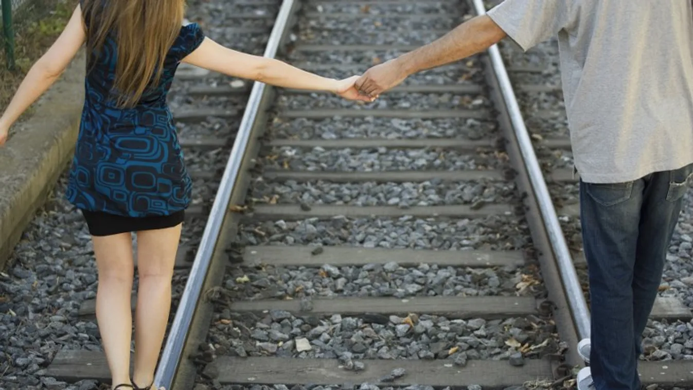 young couple rail track holding hands young adult WOMAN MAN two people young woman caucasian love trust balance beginning casual clothes outdoors day WALKING together having fun balancing two rear view cropped color image 20-25 years platform shoes wedge 