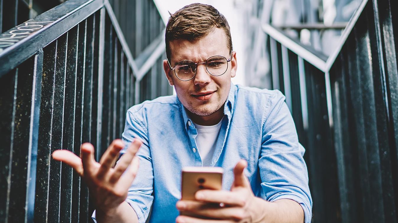 Suspicious,Caucasian,Young,Man,In,Eyeglasses,Reading,Strange,Message,On 4g internet,reading news,booking,smartphone,gadget,dislike,stair Suspicious caucasian young man in eyeglasses reading strange message on smartphone about notification with problem aft