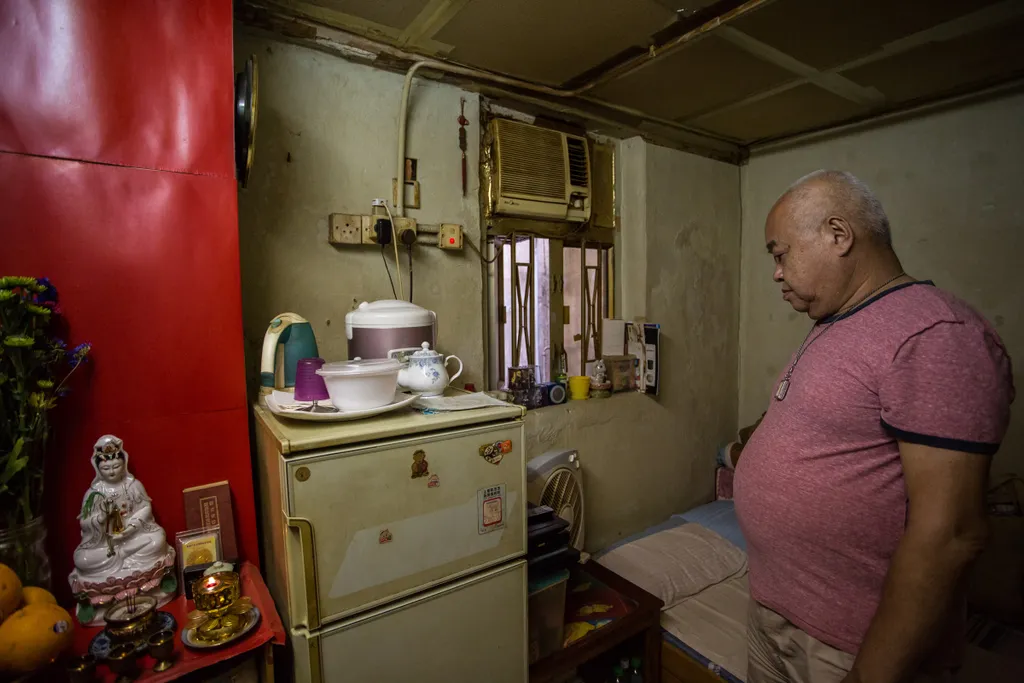 social Horizontal This picture taken on April 18, 2016 shows Mr Chan walking towards a shrine (L) next to his fridge (C) and bed (R) in his "cubicle" flat, Hong Kong 