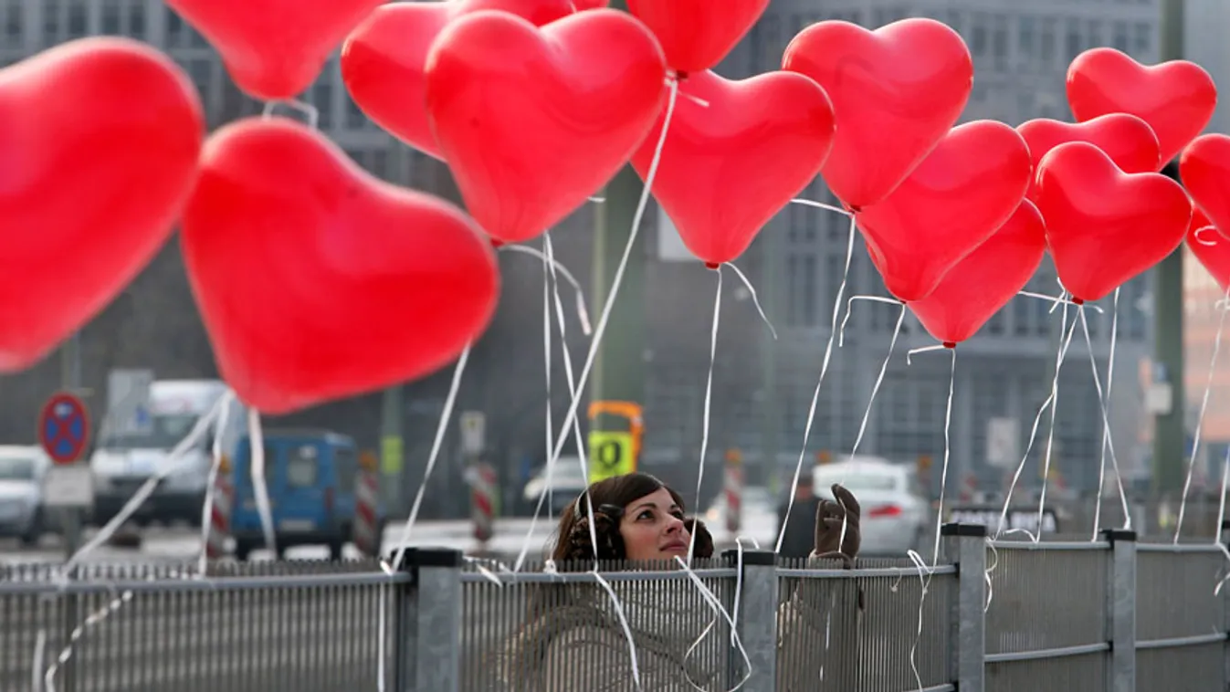 Kedvesség, egy nő szív alakú lufikat köt egy kerítésre Berlinben