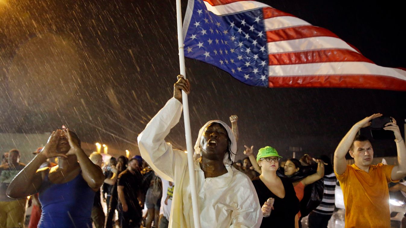 Ferguson, 2015. augusztus 10.
Tüntetők vonulnak szakadó esőben amerikai zászlóval a Michael Brown amerikai tinédzser halálának első évfordulóján tartott megemlékezés után a Missouri állambeli Fergusonban 2015. augusztus 9-én éjszaka. A demonstráció végén 