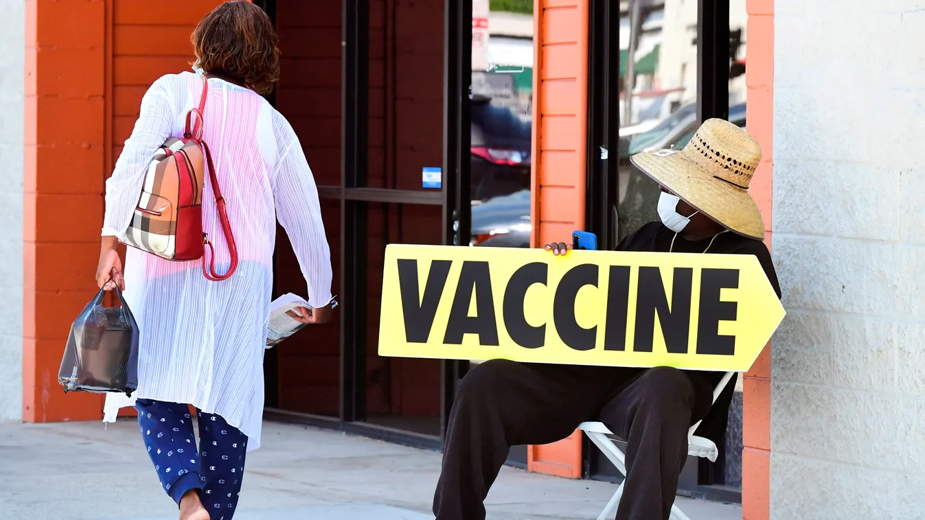 Horizontal A seated man wearing a face mask holds a sign pointing to a mobile vaccination clinic on July 16, 2021, along Crenshaw Boulevard in Los Angeles, California. - Covid cases across America are rising in all 50 states as the Delta variant spreads w