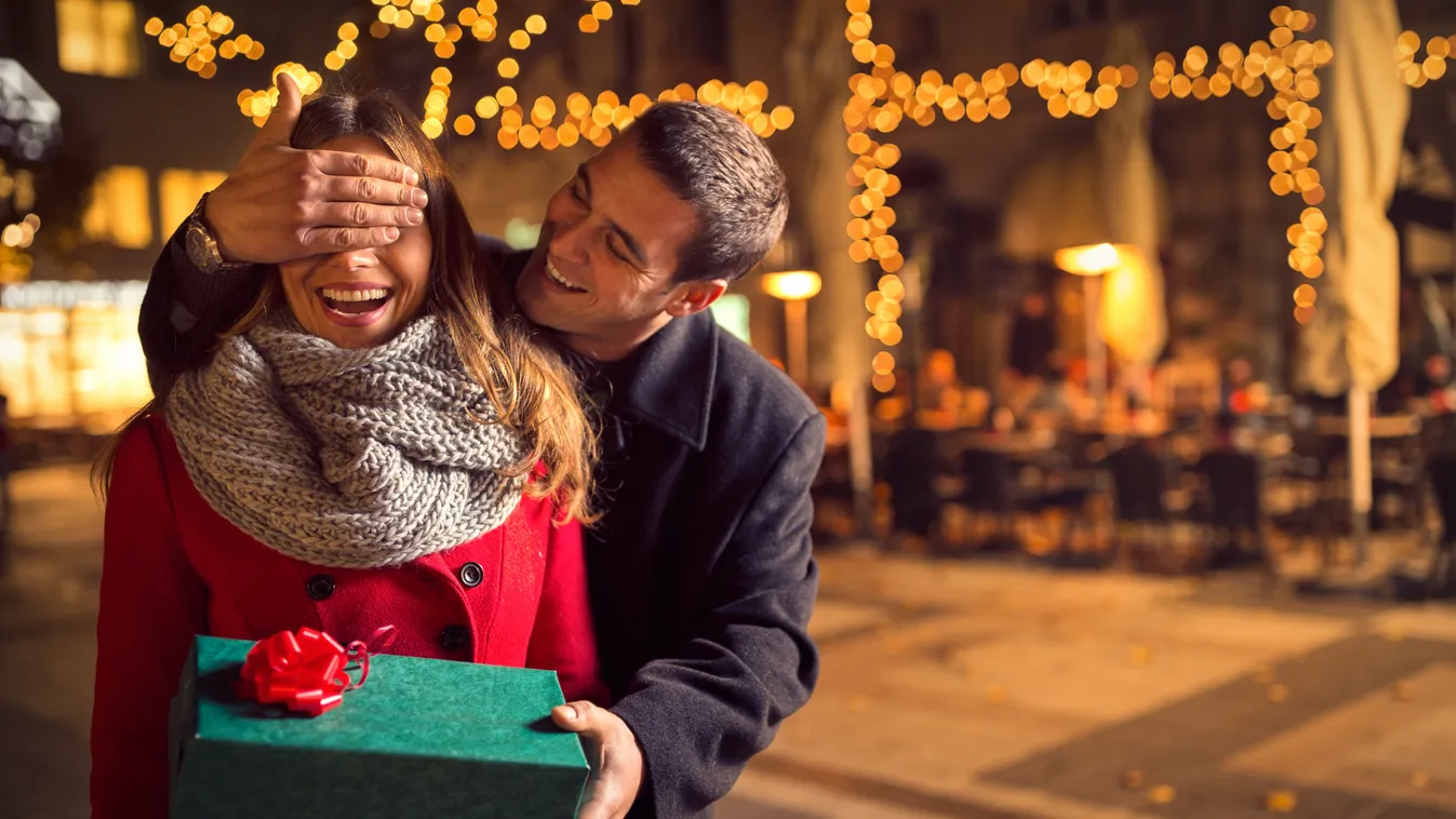 Man keeps girlfriend eyes covered while  she giving a gift Couple - Relationship New Year's Day Holiday Women City Life Celebration Dating Flirting Facial Expression Anniversary Valentine's Day - Holiday Date Young Adult Smiling Decorating Street Light Fu