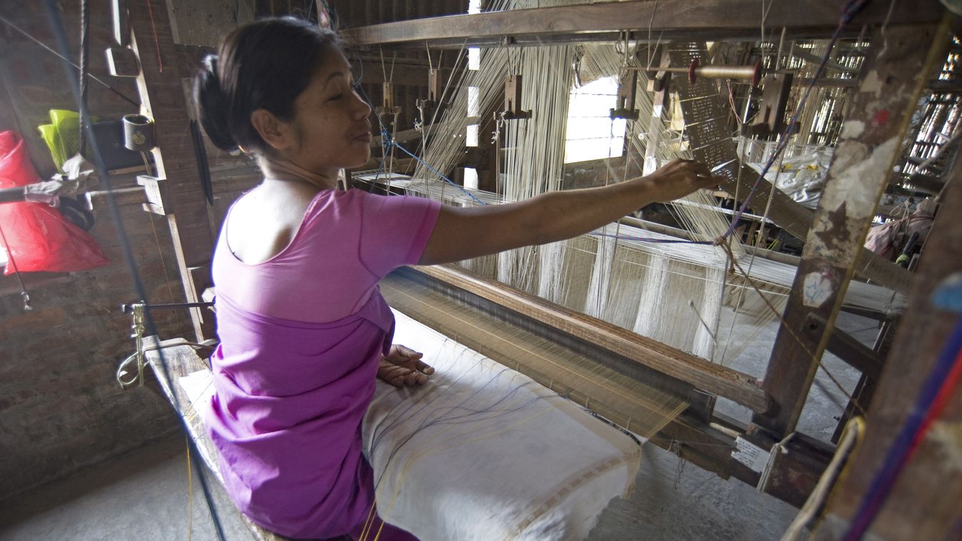 Woman at village silk loom weaving Assam Muga natural undyed silk in Sualkuchi, Assam, India, Asia color image travel photography travel destinations day indoors people WOMAN women work craft crafts factory factories interiors WEAVING WEAVER weavers LOOM 