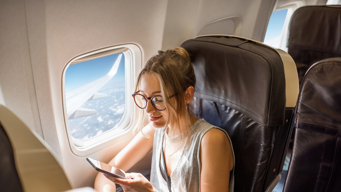 Young,Woman,Sitting,With,Phone,On,The,Aircraft,Seat,Near plane 