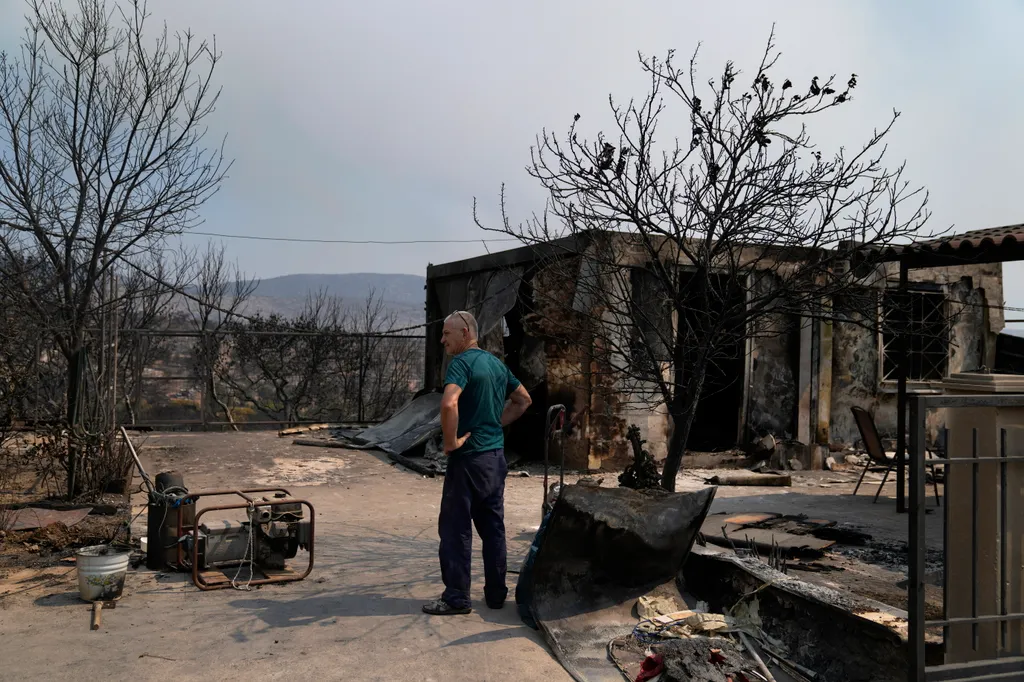 tűzoltó tomboló erdőtűz Görögország ház előtt egy férfi az Athéntól nyugatra fekvő Mandrában 2023. július 19-én. Az Európai Unió egyik polgári védelmi mechanizmusának keretében Franciaország és Olaszország két-két tűzoltó-repülőgépet 