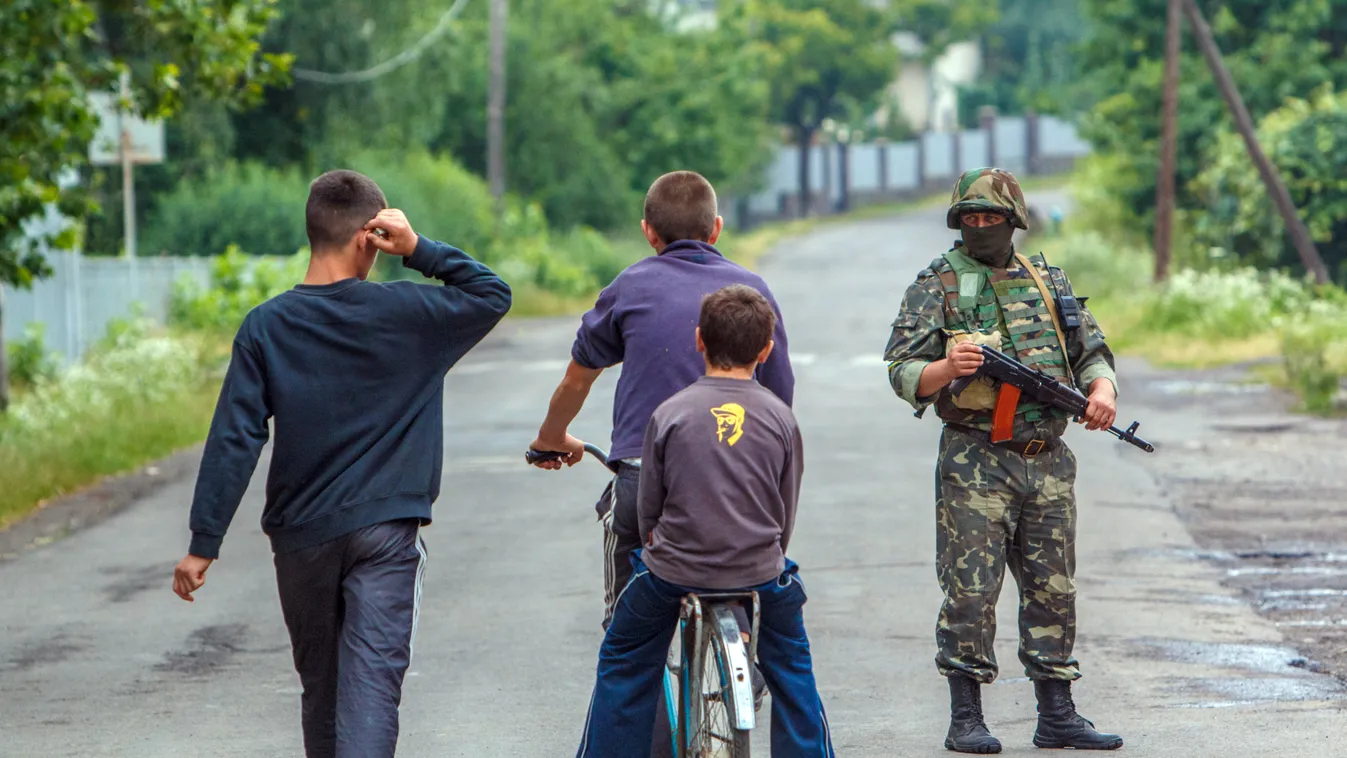 Gyerekek mennek el kommandósok ellenőrző pontja mellett Munkácson . Tűzharc tört ki július 11-én a város egyik sportlétesítménynél a Jobboldali Szektor (PSZ) szélsőséges szervezet fegyveresei és az ukrán parlament egyik kárpátaljai képviselőjének emberei,
