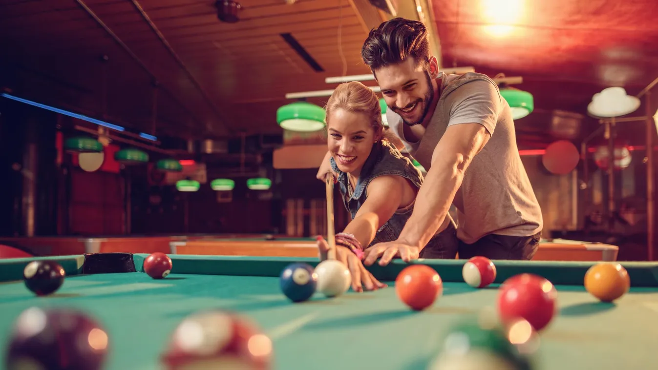 Young happy couple enjoying in a billiard game together. Couple - Relationship Pub Pool Hall Pool Ball Leisure Activity Women Females Men Males Two People Snooker and Pool Hobbies Dating Flirting Aiming Lens Flare Pool Cue Young Adult Adult Smiling Playin