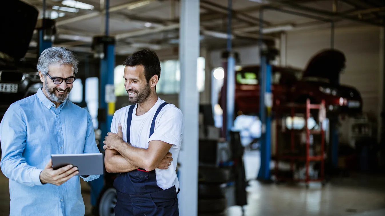 Happy manager and mechanic using digital tablet in auto repair shop. Mid adult manager and auto mechanic cooperating while reading plans on touchpad in a workshop. 