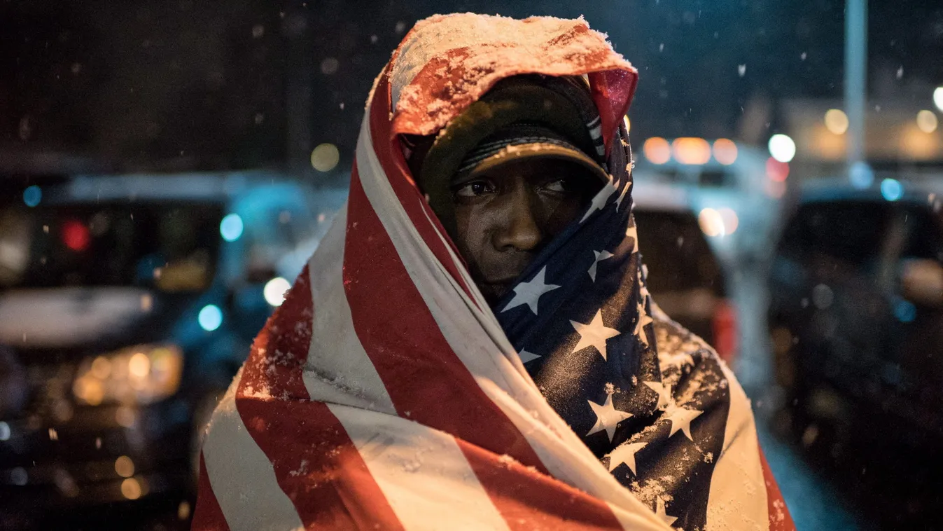 St. Louis, Ferguson zavargások
Amerikai zászlóba burkolózott tüntető áll a rendőrség épülete előtt hóesésben a Missouri állambeli St. Louis Ferguson városrészében 2014. november 26-án. A városban két napja zavargások kezdődtek azt követően, hogy a vádeskü