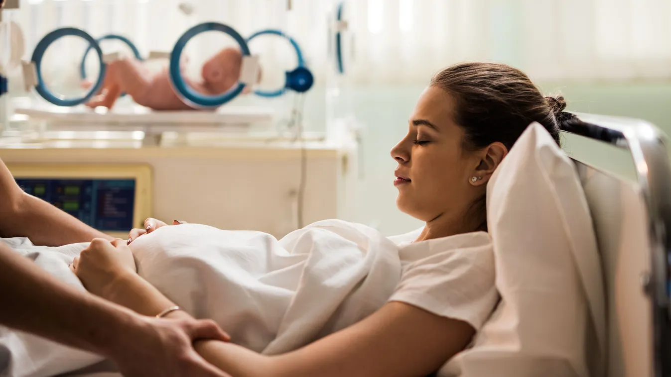 Young mother resting in maternity room after childbirth. Hands On Stomach Leisure Activity Women Females Men Males Two People Clinic Eyes Closed Hospital Nursery Delivery Room Incubator Young Adult Adult Child Lying Down Resting Caucasian Ethnicity New Li