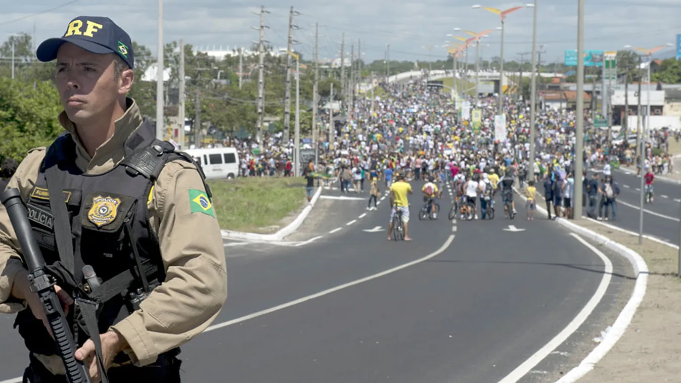 Brazília, Fortaleza, fegyveres rendfenntartó az utcán háttérben a fociberuházások miatt tüntető brazilok