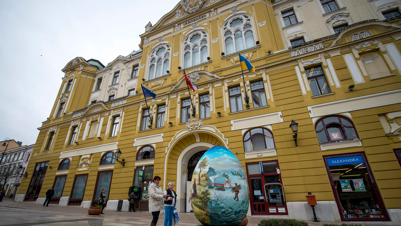 Érdeklődők nézik az ember nagyságú hímes tojást Pécsen, a Széchenyi téren, a városháza előtt. A tojást Dráva menti festőművészek díszítették, és a horvátországi Kapronca-Körös megye ajándéka Pécs lakóinak és az idelátogató turistáknak. 