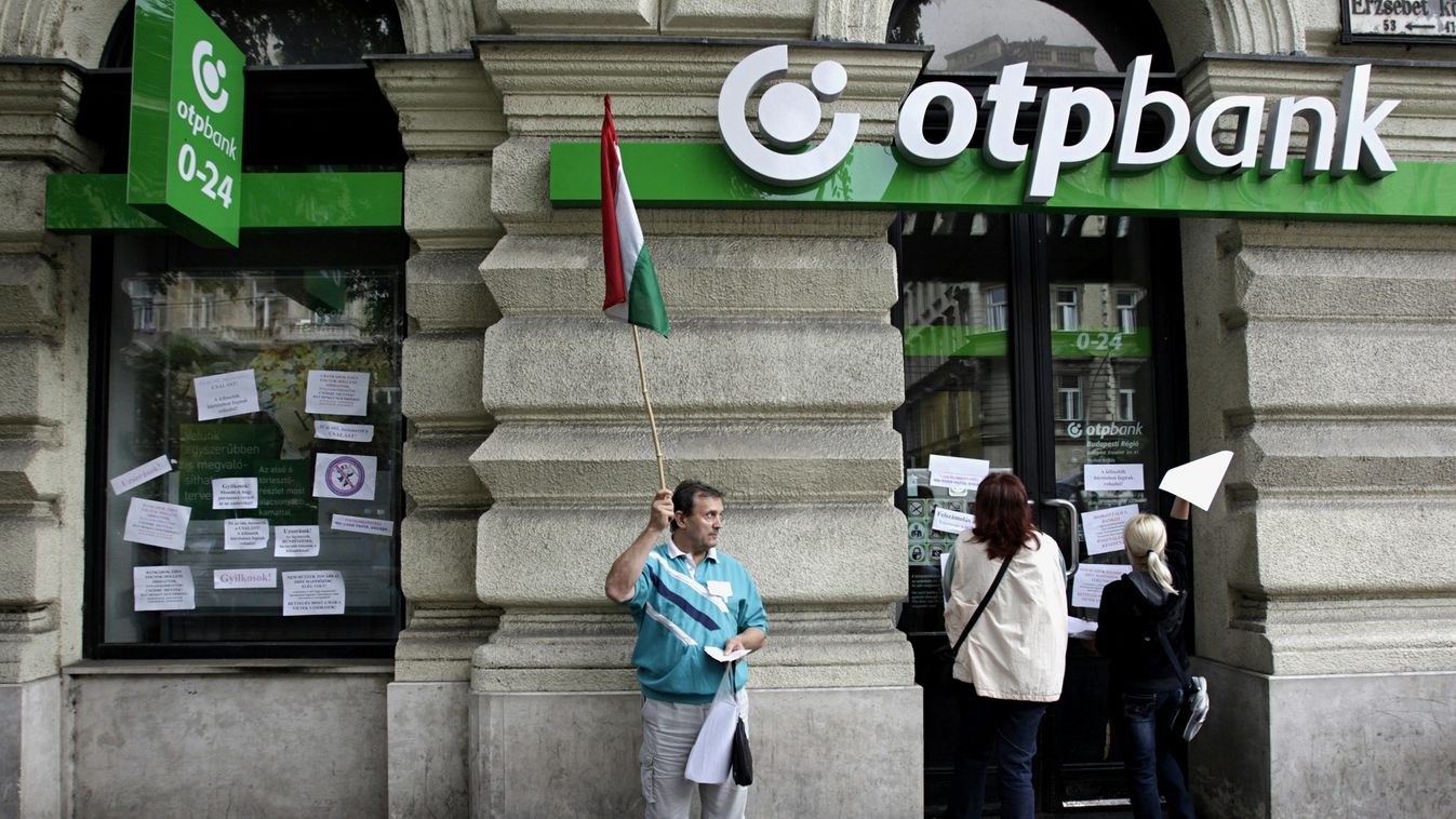 további százezrekre számíthatnak a devizahitelesek, Demonstrálók feliratokat ragasztanak fel egy OTP-bankfiók ablakára 2013. augusztus 27-én 