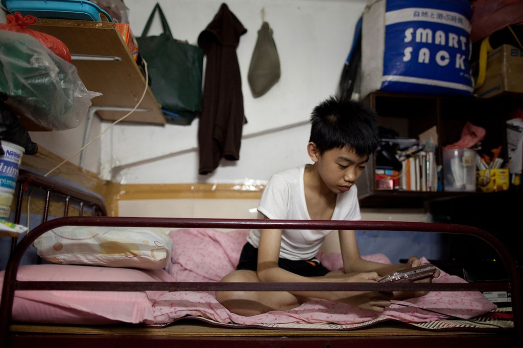 Horizontal A boy plays a computer game as he sits on his bed in a  cubicle in Hong Kong on May 20, 2011.  Amid rising inflation many cage or cubicle home dwellers risk being subjected to rent increases despite paying a similar price per square foot as som
