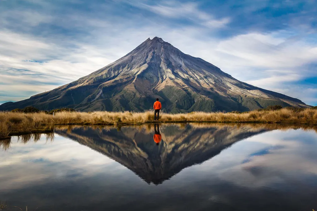 az emberek túrázás közben 
 big,perfect,hut,scenic,climb,cloud,beautiful,high,mountain,west, A mountaineer with an orange dress in a symmetric picture looking to the taranaki volcano in the north island of new zealand and wit 