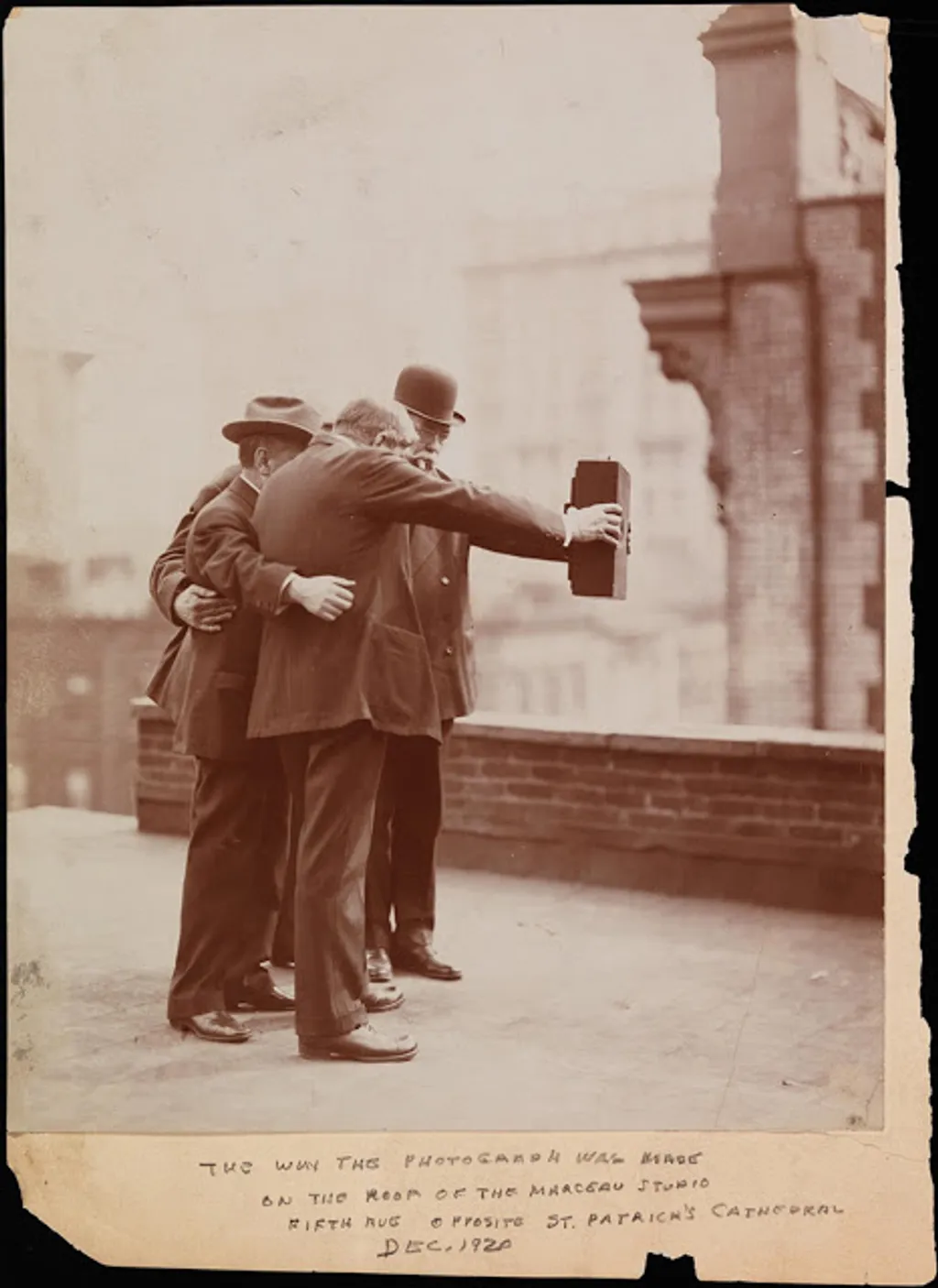 selfie galéria Side view of photographers posing together for a photograph on the roof of Marceau’s Studio, while Joseph Byron holds one side of the camera with his right hand and Ben Falk holds the other side with his left hand. 