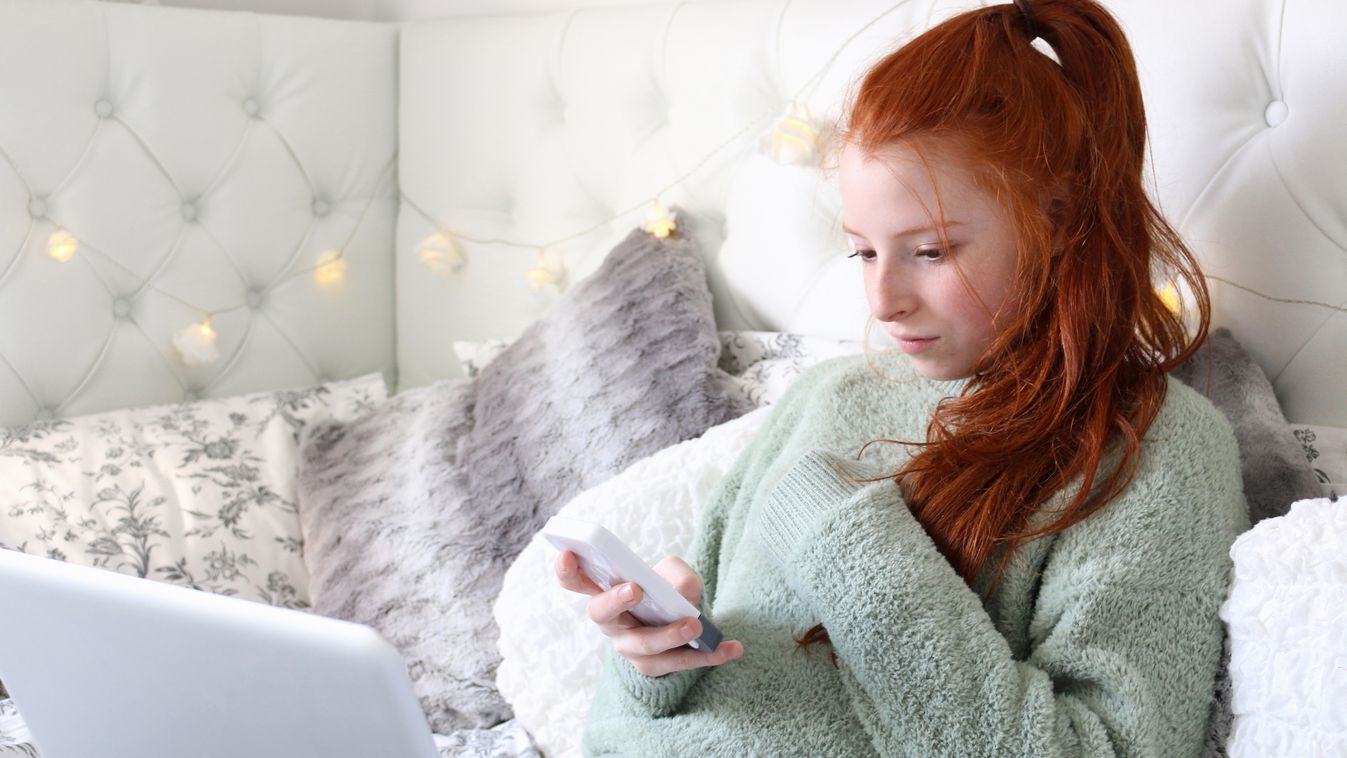 Image of teenage girl in bedroom using laptop and phone Using Laptop Wireless Technology Headboard Real People Serene People Computer Using Phone Using Computer Text Messaging Teenage Girls Females Surfing the Net Multi-Tasking Fashion Model Reclining Loo