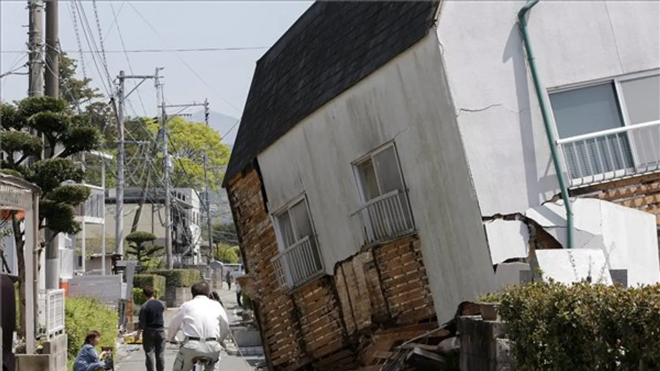 Megdőlt lakóház mellett kerékpározik egy férfi a délnyugat-japáni Kumamoto tartományban fekvő Masiki városban. 