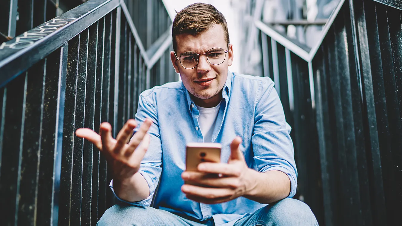 Suspicious,Caucasian,Young,Man,In,Eyeglasses,Reading,Strange,Message,On 4g internet,reading news,booking,smartphone,gadget,dislike,stair Suspicious caucasian young man in eyeglasses reading strange message on smartphone about notification with problem aft