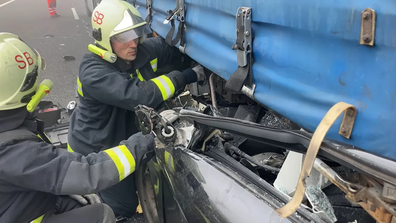 Az M7-es autópályán 2024. február 25-én reggel történt tömegkarambol egyik résztvevőjét próbálják kiszabadítani a kocsijából, ami egy teherautó alá szorult