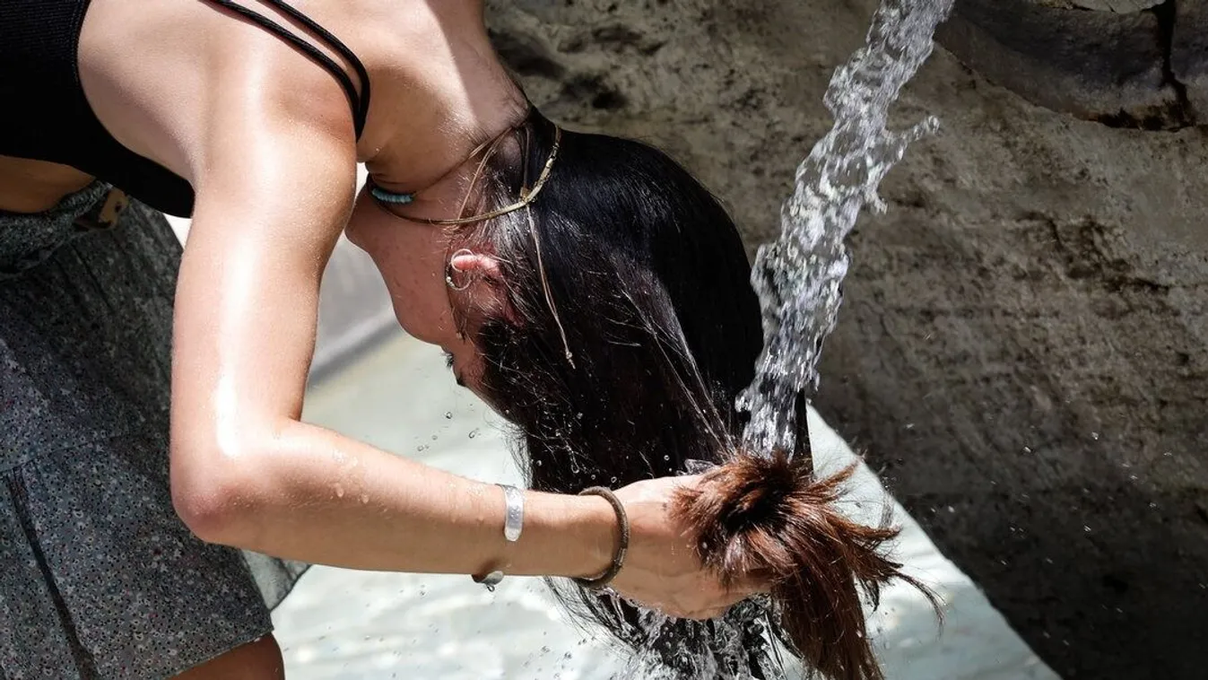 Egy nő egy kútnál vizezi be haját, hogy így frissüljön fel a hőségben (illusztráció)