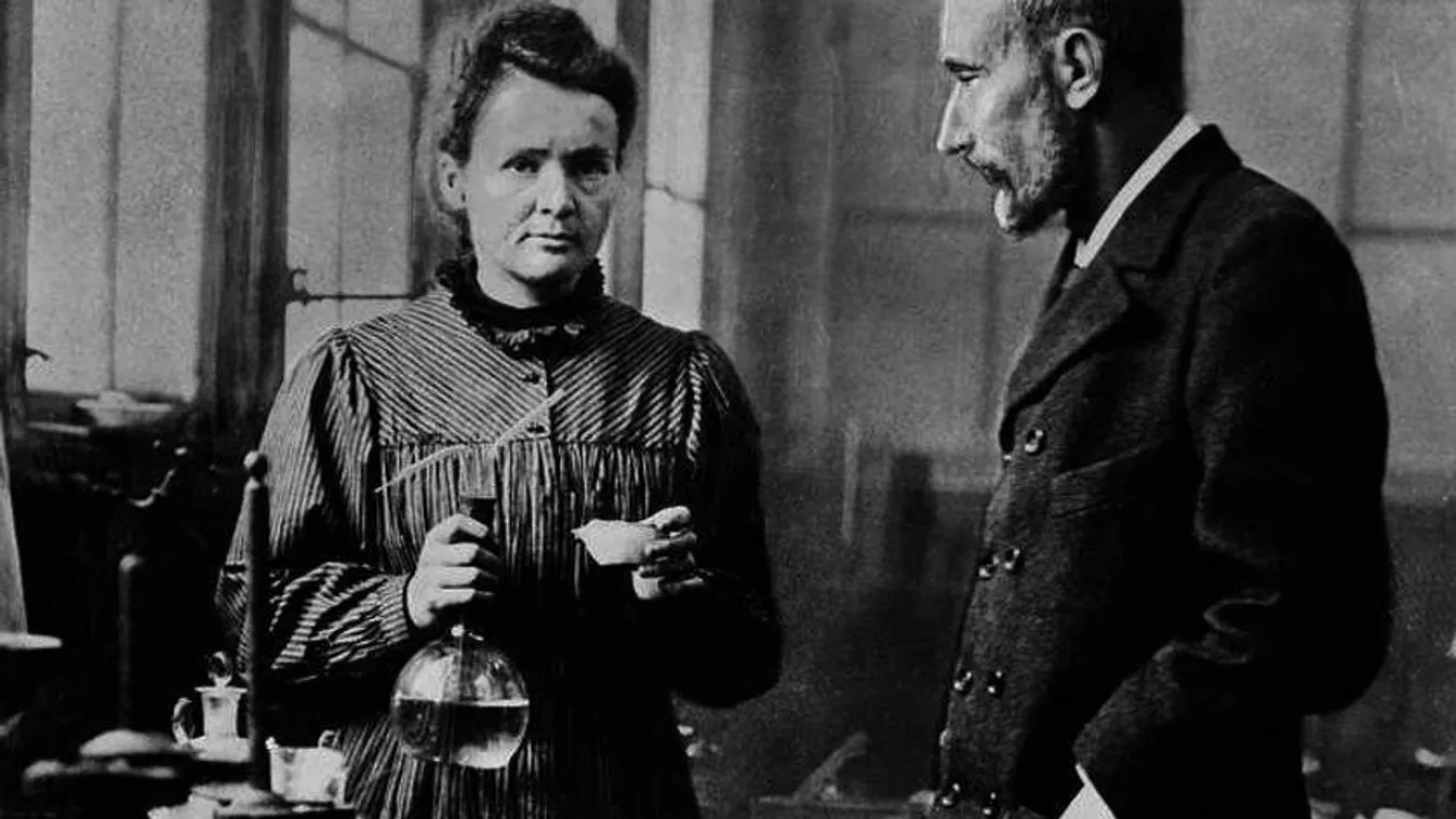 Marie Curie kezében lombikot tart, mellette férje Pierre Curie