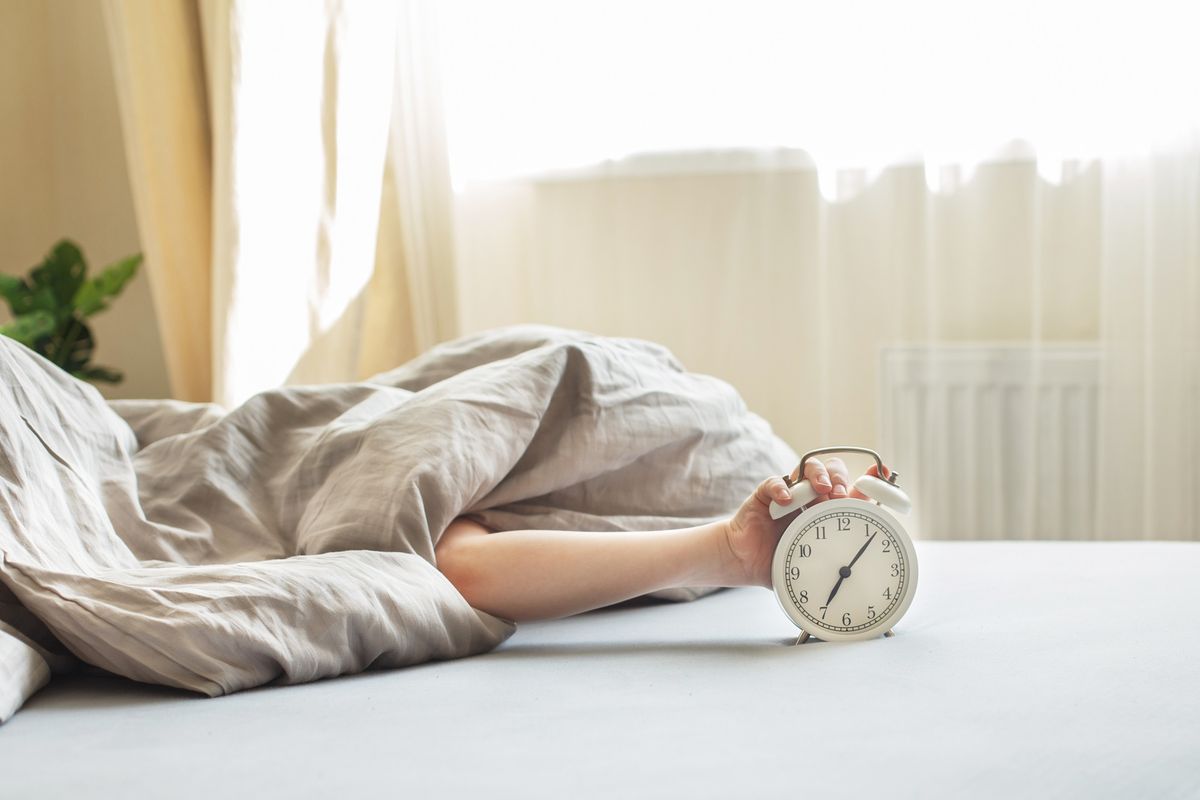 boy lying on the bed under a blanket and stopping alarm clock in the morning. childs hand reaching for the alarm clock to turn it off.