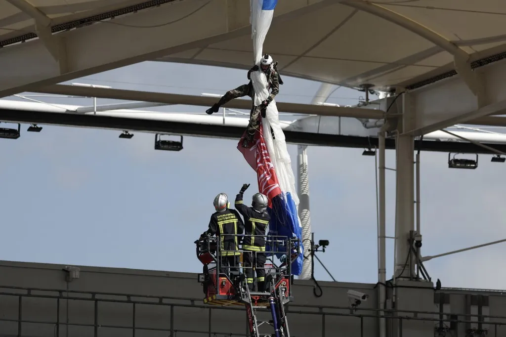 Firefighters work to rescue an air force parachutist (Top) whose canopy is jammed on the roof of the stadium prior to the European Rugby Champions Cup last 16 rugby union match between Stade Toulousain Rugby (Toulouse) and Sale Sharks at the Stadium in Toulouse, south-western France, on April 6, 2025. An air force parachutist, who was supposed to bring the match ball onto the pitch at Toulouse Stadium from the air, had to be unhooked from the roof of the stadium before the start of the Champions Cup Round of 16 match, which was delayed on April 6, 2025. Five minutes before kick-off of the match against England's Sale, scheduled for 4 p.m., a gust of wind knocked the parachutist off course, sending him towards the roof where his canopy became caught in the stadium structure. (Photo by Valentine CHAPUIS / AFP)