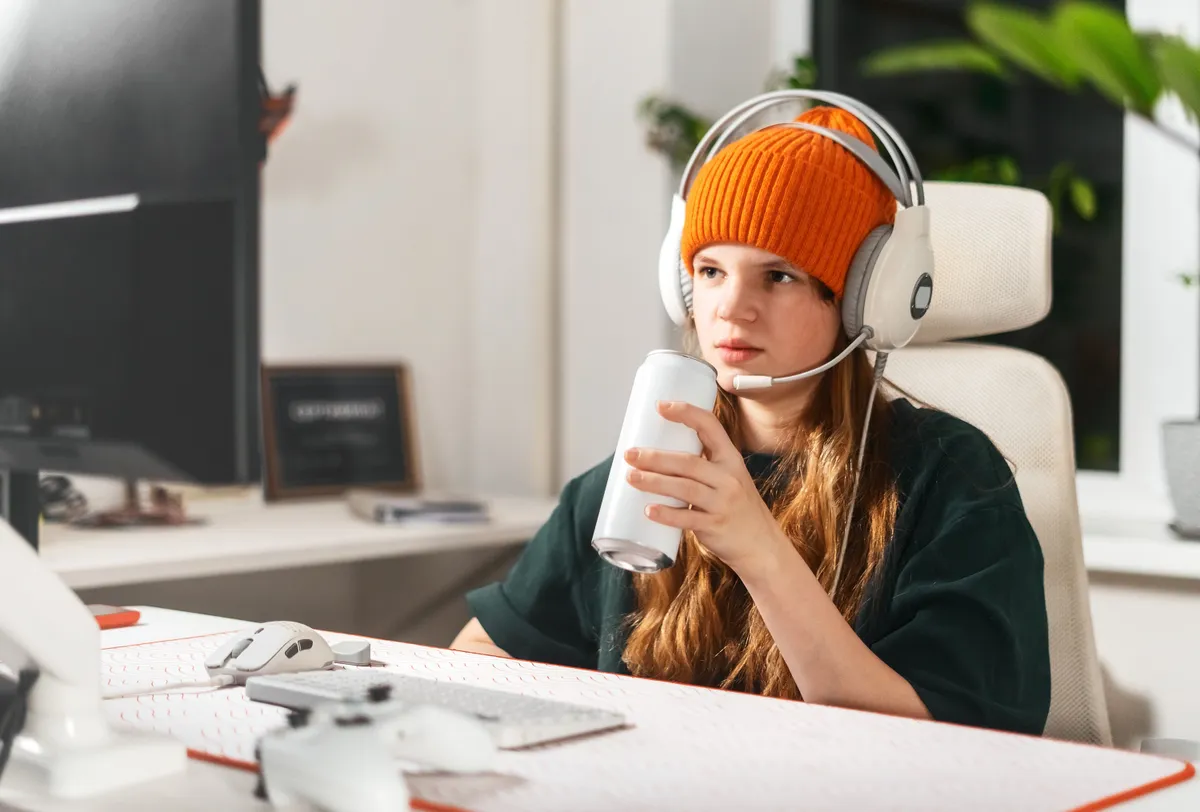 Gamer girl takes break from an intense gaming session, sitting her computer desk in cozy chair while sipping energy drink. Concept digital hobby and love for video games, fueled by caffeine and focus