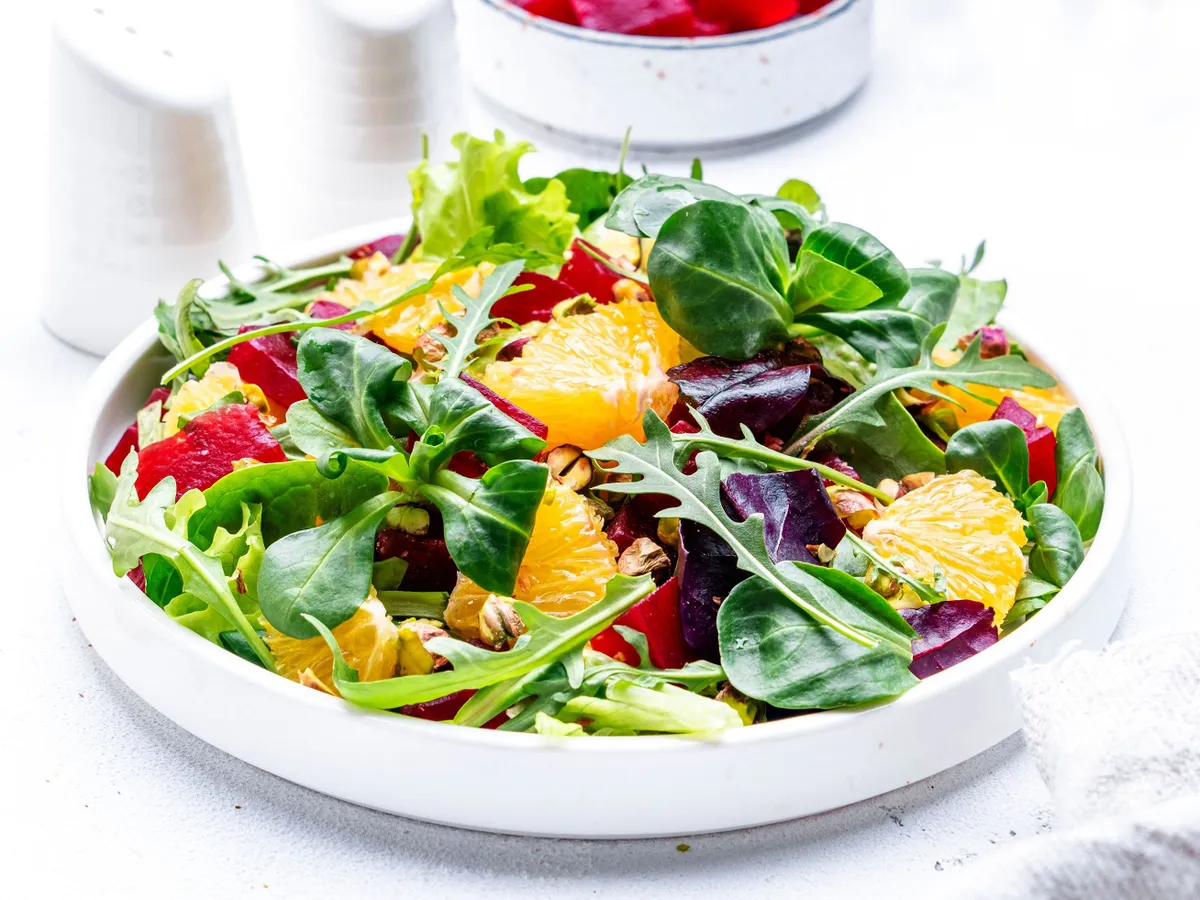 Beetroot and orange salad with arugula, lamb lettuce, mini chard and pistachios, white table, copy space.. Fresh useful dish for healthy eating