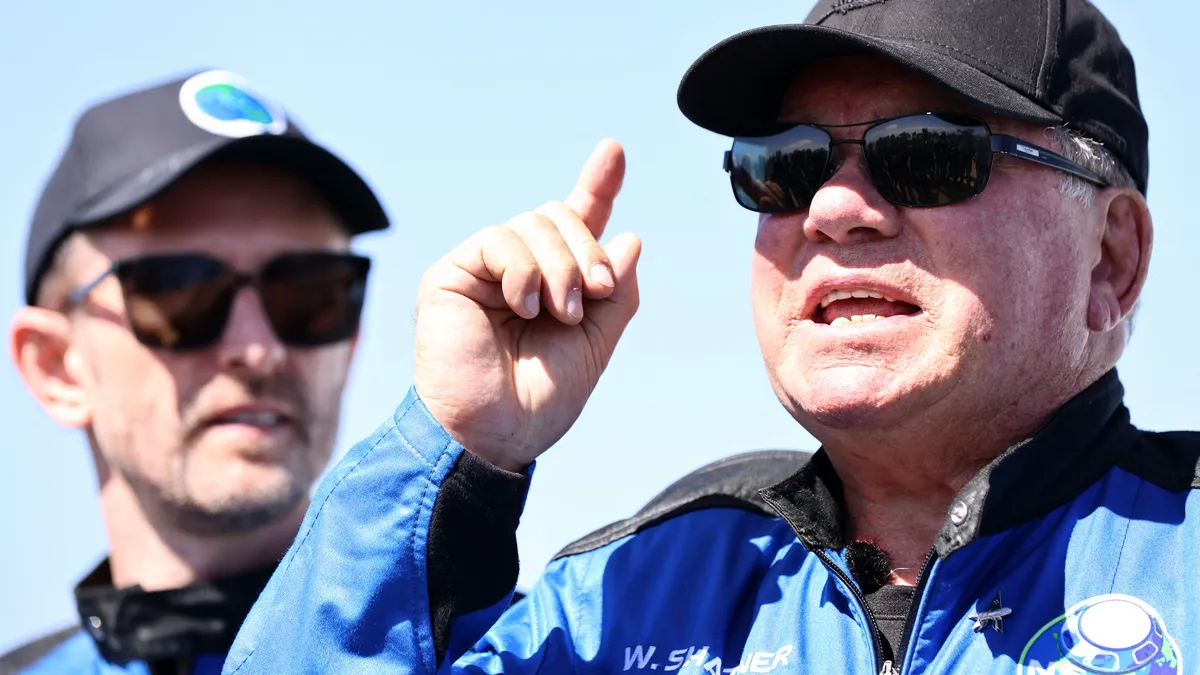 VAN HORN, TEXAS - OCTOBER 13: Star Trek actor William Shatner speaks as Planet Labs co-founder Chris Boshuizen looks on during a media availability on the landing pad of Blue Origins New Shepard after they flew into space on October 13, 2021 near Van Horn, Texas. Shatner became the oldest person to fly into space on the ten minute flight. They flew aboard mission NS-18, the second human spaceflight for the company which is owned by Amazon founder Jeff Bezos.   Mario Tama/Getty Images/AFP (Photo by MARIO TAMA / GETTY IMAGES NORTH AMERICA / Getty Images via AFP)