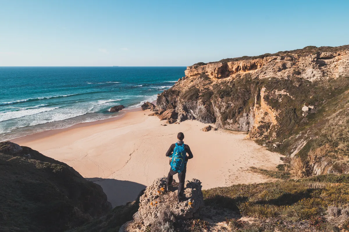 Passionate backpacker looks out over sandy beach of Praia da Angra da Cerva on the Atlantic coast near Vila Nova de Milfontes, Odemira, Portugal. In the footsteps of Rota Vicentina. Fisherman trail.