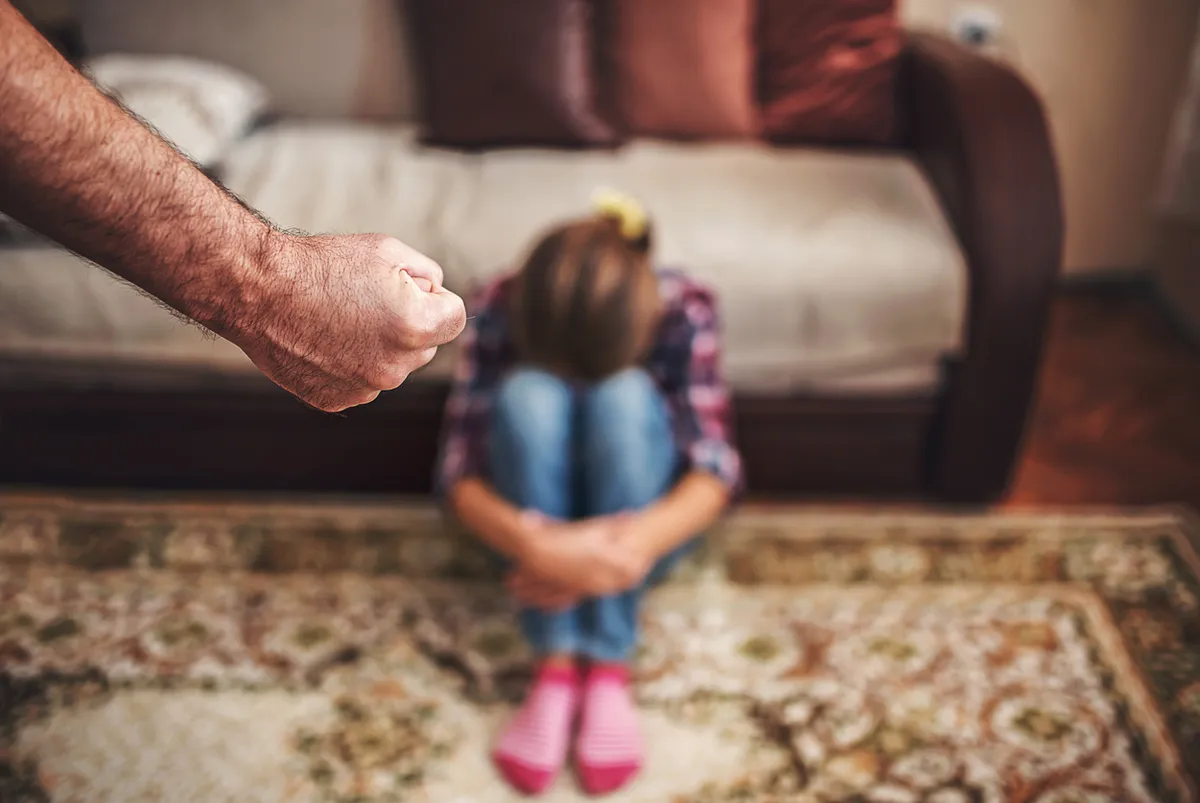 Violence against children. Crying little girl sitting on the floor while man clenching fist in anger