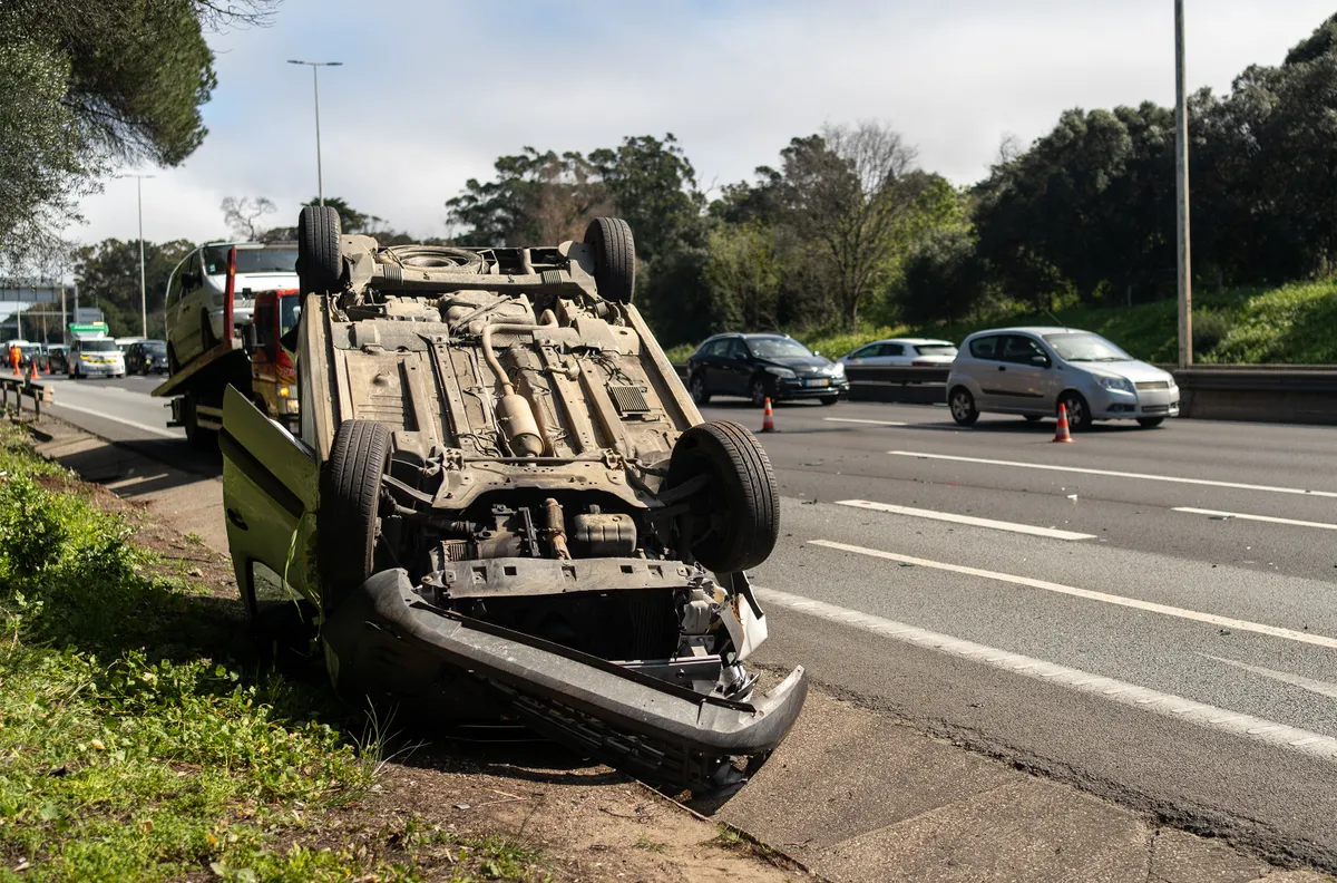 Damaged wrecked car after collision lying upside down on roadside. Busy city street with car rolled over during daytime. Car accident