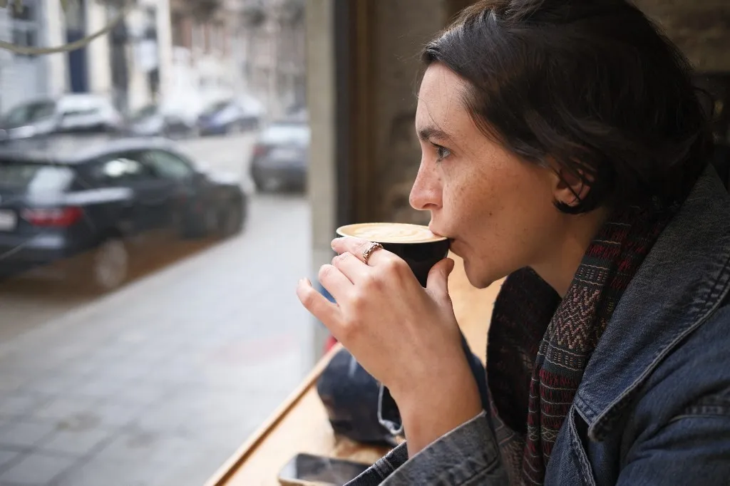 A young woman sipping coffee while gazing outside a window in an urban café. (Photo by LB Studios / Connect Images / Connect Images via AFP)