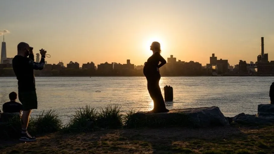 A pregnant woman poses for photos before the Manhattan city skyline at sunset in a park in Williamsburg, New York on April 20, 2021. (Photo by Ed JONES / AFP) várandós, terhes