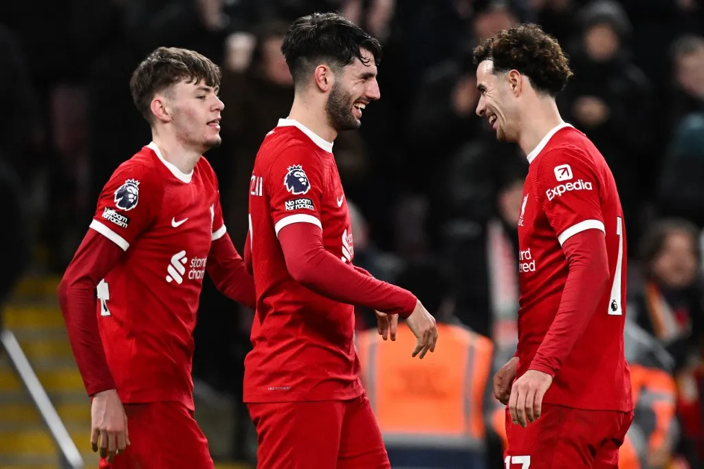 Liverpool's Hungarian midfielder #08 Dominik Szoboszlai (C) celebrates with Liverpool's Northern Irish defender #84 Conor Bradley (L) and Liverpool's English midfielder #17 Curtis Jones (R) after scoring his team third goal during the English Premier League football match between Liverpool and Chelsea at Anfield in Liverpool, north west England on January 31, 2024. (Photo by Paul ELLIS / AFP) / RESTRICTED TO EDITORIAL USE. No use with unauthorized audio, video, data, fixture lists, club/league logos or 'live' services. Online in-match use limited to 120 images. An additional 40 images may be used in extra time. No video emulation. Social media in-match use limited to 120 images. An additional 40 images may be used in extra time. No use in betting publications, games or single club/league/player publications. / 