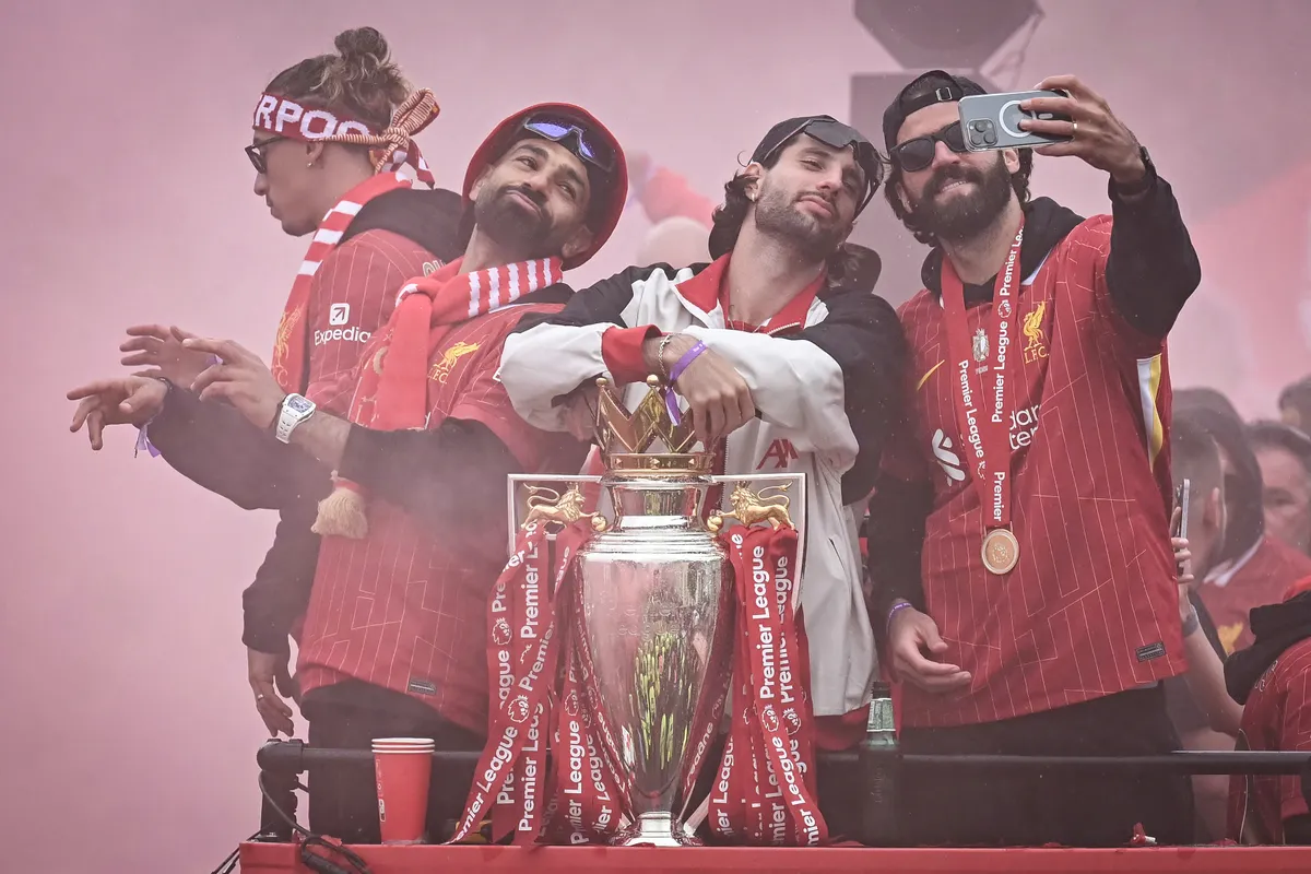 (from L) Liverpool's Egyptian striker #11 Mohamed Salah, Liverpool's Hungarian midfielder #08 Dominik Szoboszlai and Liverpool's Brazilian goalkeeper #01 Alisson Becker pose for a selfie as they celebrate with the Premier League trophy during an open-top bus victory parade for Liverpool's Premier League title win, in Liverpool, north-west England on May 26, 2025. (Photo by Paul ELLIS / AFP)