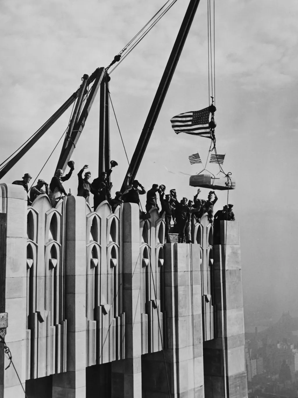 Az első felhőkarcolók építése,  Construction workers cheer as the last piece of limestone, decorated with two small American flags, is set in place on the parapet of the RCA Building, part of Rockefeller Center in New York, December 7th 1932. (Photo by Ke
