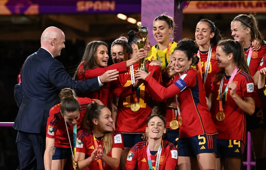 Spain's Queen Letizia (2L) holds the trophy next to FIFA President Gianni Infantino as Spain's players celebrate after winning the Australia and New Zealand 2023 Women's World Cup final football match between Spain and England at Stadium Australia in Sydney on August 20, 2023. (Photo by WILLIAM WEST / AFP), foci-vb