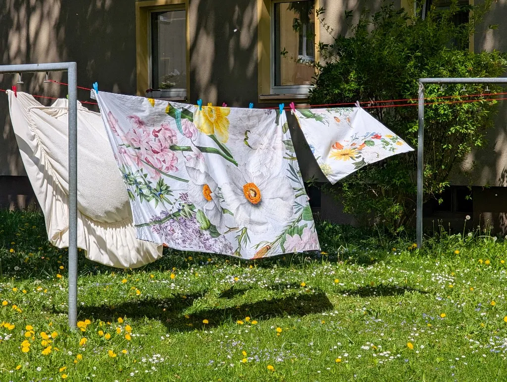 ágynemű Freshly washed bed linens and textiles hang on a clothesline to dry in the garden of a residential building in Munich, Germany, on April 28, 2025. The linens feature floral patterns and dry naturally in the sun among blooming spring grass and flowers. (Photo by Michael Nguyen/NurPhoto) (Photo by Michael Nguyen / NurPhoto / NurPhoto via AFP)