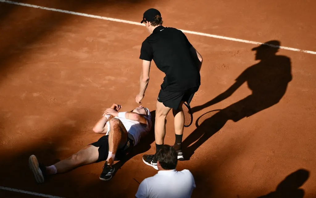 teniszsztár, Netherland Jesper De Jong (L) lies on the ground as Italy's Jannik Sinner help him during their round of 16 men's singles match of the WTA Rome Open tennis tournament at Foro Italico in Rome on May 12, 2025. (Photo by Marco BERTORELLO / AFP)