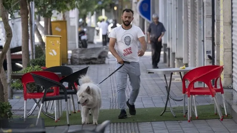 A young Iranian man and his pet are walking along a sidewalk, amidst the early presidential election campaigns, in downtown Tehran, Iran, on June 17, 2024. Iranian people are casting their ballots to select Iran&#039;s new President on June 28th, as late president Ebrahim Raisi died in a helicopter crash two years before the end of his presidency. (Photo by Morteza Nikoubazl/NurPhoto) (Photo by Morteza Nikoubazl / NurPhoto via AFP)