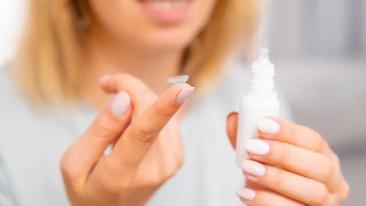 Woman holding contact lens on the finger and eye drop in her hand. Eyecare concept.