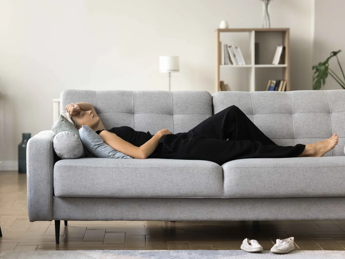 Tired elderly lady rest at home after long difficult work day lie on soft couch in relaxed pose sleep nap daydream. Exhausted aged female lying on sofa at living room feel headache migraine need quiet