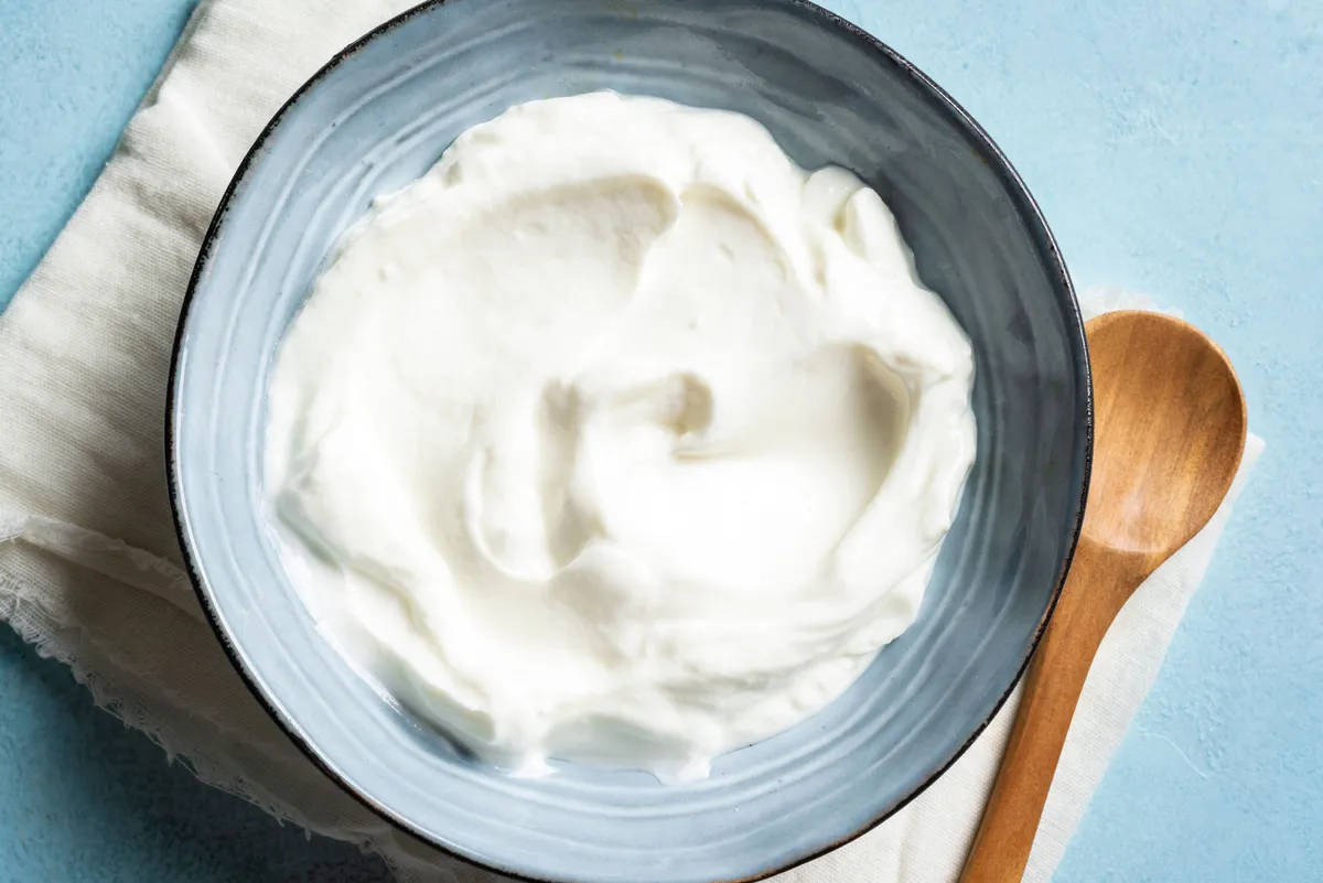 Homemade Greek Yogurt in blue bowl close up, top view. Organic plain greek yogurt, labneh cream cheese, sour cream for healthy breakfast.