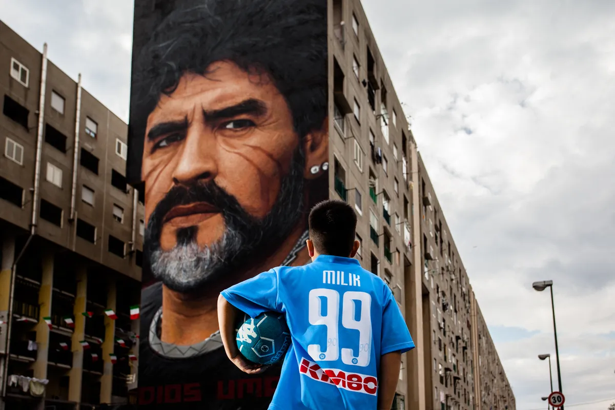 A children that dribble of Taverna Del Ferro, San Giovanni a Teduccio, peripheral of Naples EST on March 29, 2017 in front a Graffiti Revolucionario by Jorit, hand painted on wall with spray cans,  Diego Armando Maradona on wall of a building. (Photo by Paolo Manzo/NurPhoto) (Photo by Paolo Manzo / NurPhoto via AFP)