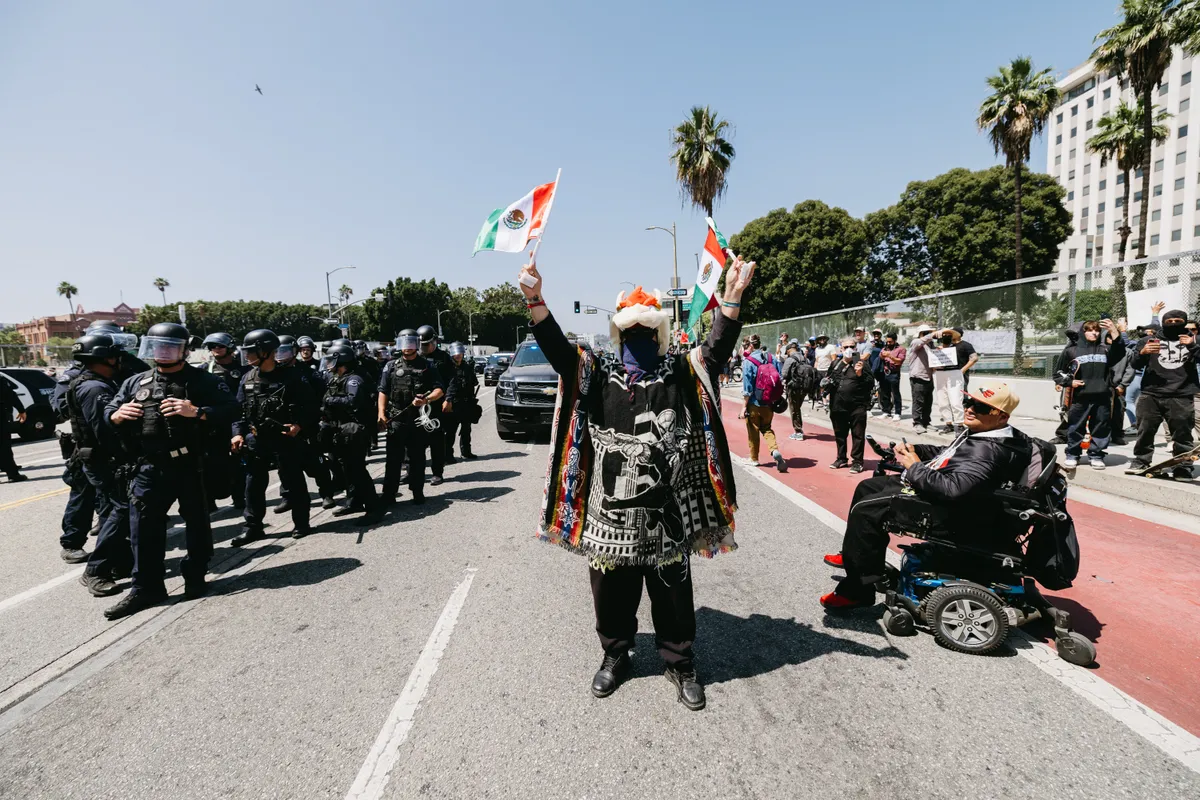 A demonstrator holds two Mexican flags, as they face a line of law enforcement officers during a protest in Los Angeles, California, on June 8, 2025. Following a series of aggressive federal immigration operations in Los Angeles, tensions escalated when Immigration and Customs Enforcement (ICE) agents conducted a high-profile raid on a Home Depot location. The raid sparked widespread protests across the city, where demonstrators decried the targeting of immigrant communities and the separation of families. Clashes soon broke out between protesters and federal agents, prompting U.S. President Donald Trump to deploy 2,000 National Guard troops to the city, a move harshly criticized by California officials, including the governor, as "purposefully inflammatory." (Photo by David Pashaee / Middle East Images via AFP)